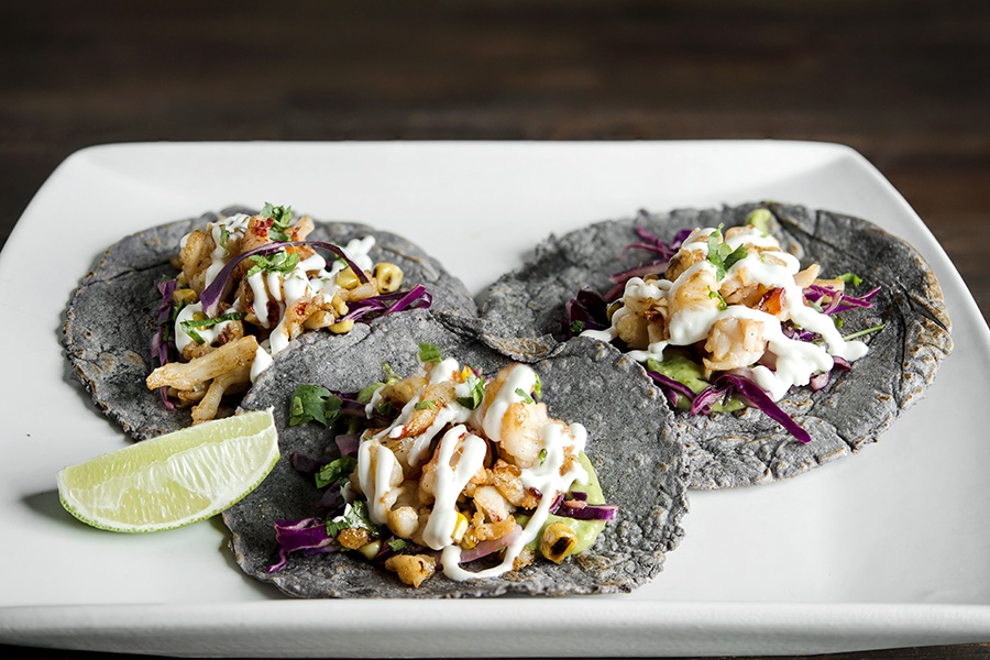 Three lobster tacos sit on a plate. The tortillas are thick and gray.