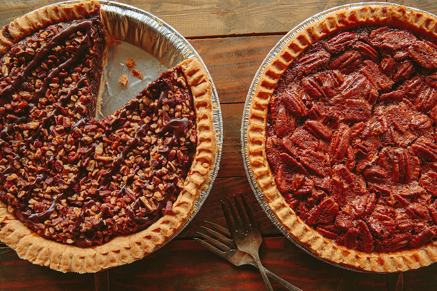 Overhead view of two pies on a wooden surface. One is pecan.
