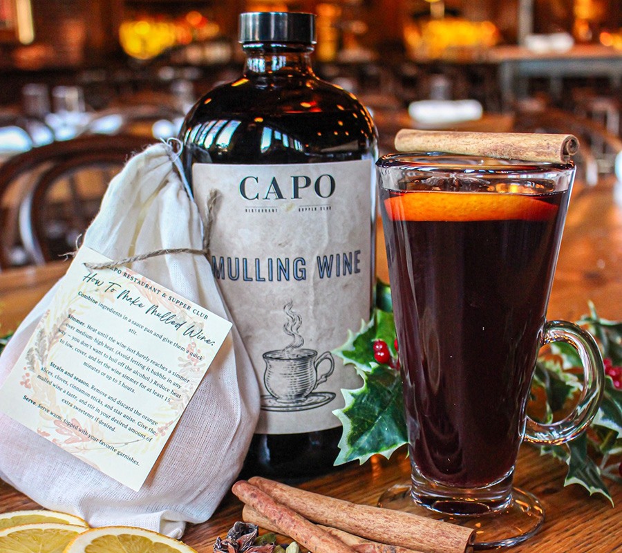 A bottle of mulling wine, a package of spices, and a mug of hot mulled cider.