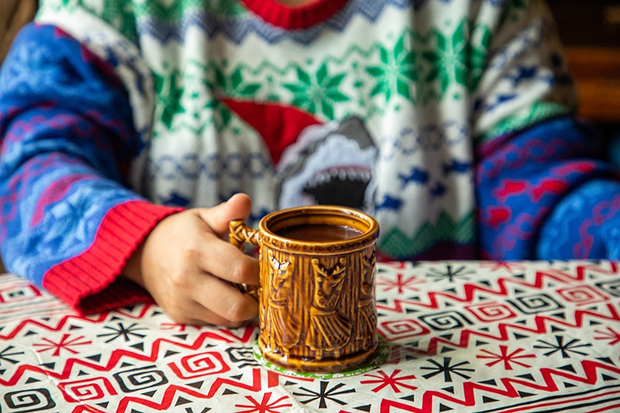 A person in a Christmas sweater holds a tiki mug.