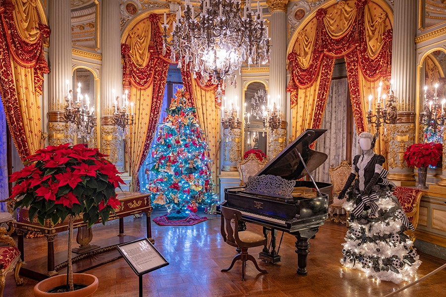 An elegant music room in a fancy mansion is decorated for Christmas and features a grand piano.