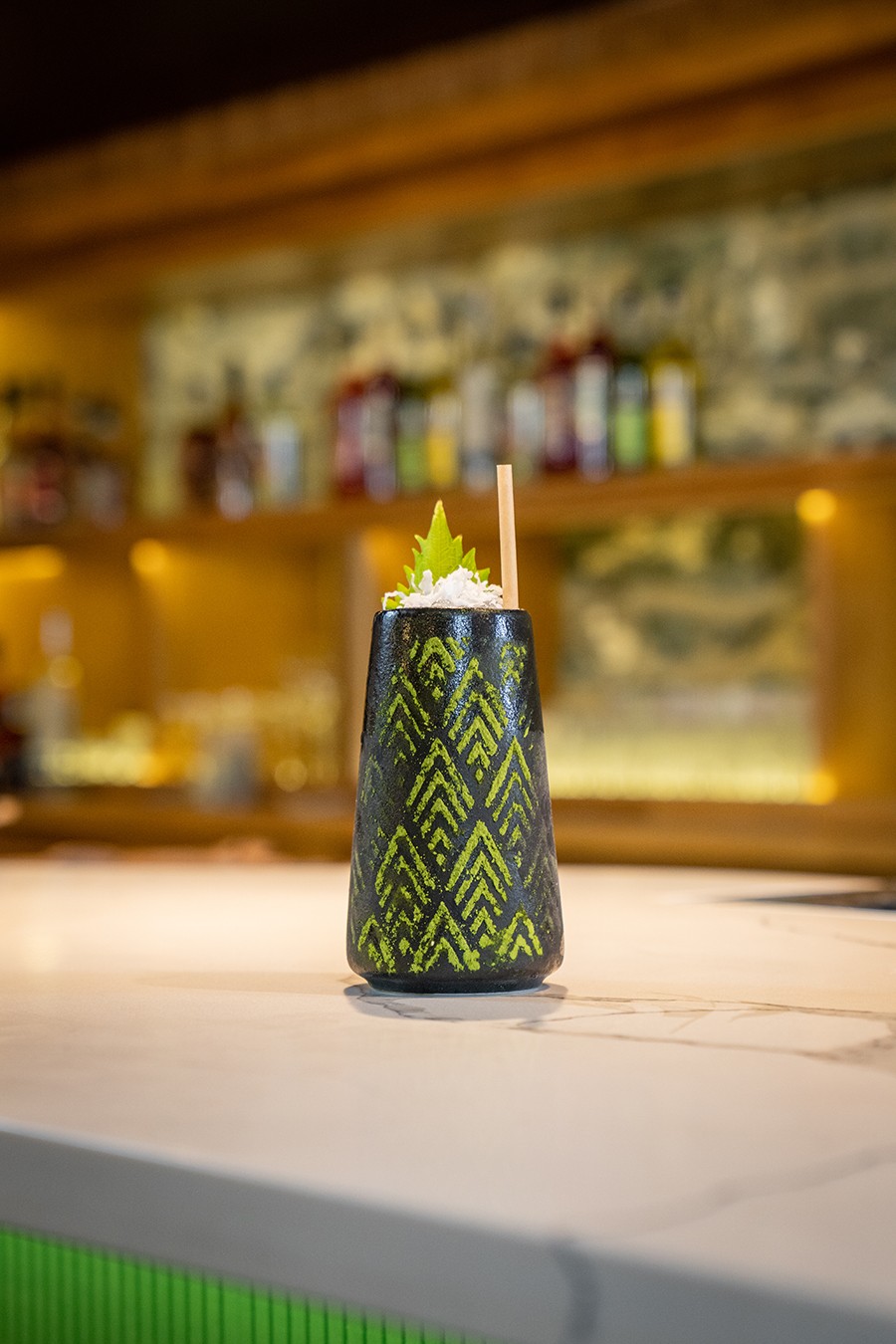 A tropical cocktail is served in a glass decorated with green arrow-like shapes.