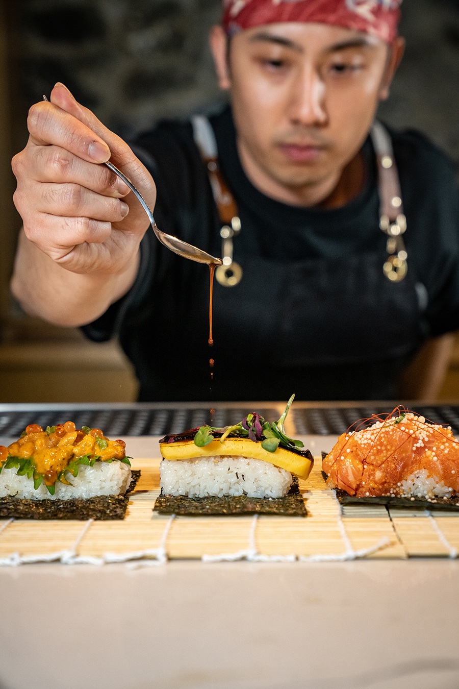 A sushi chef places the finishing touches on several pieces of sushi.