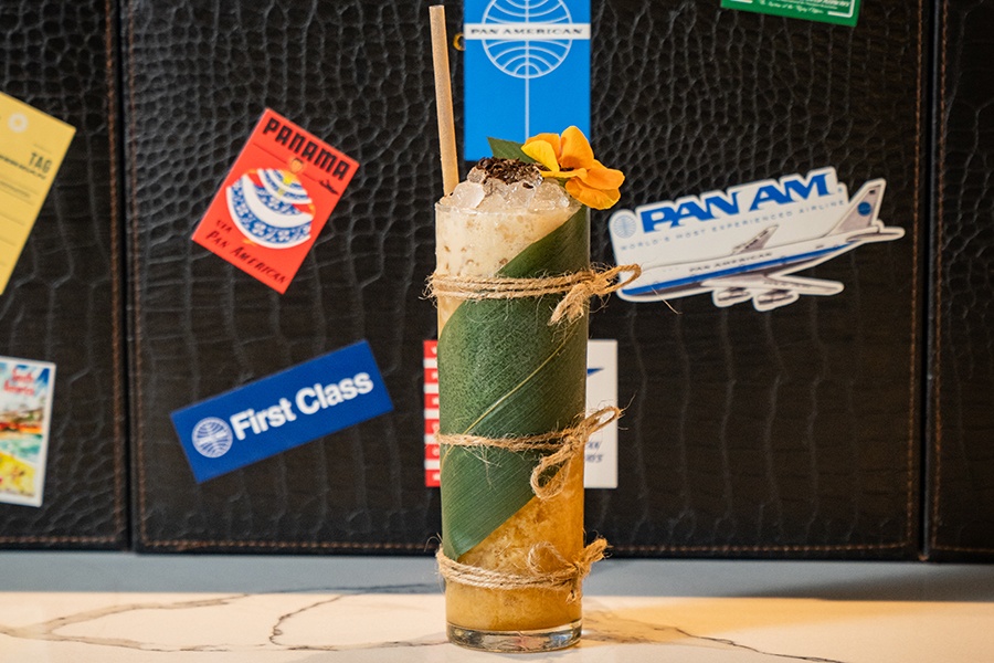 A banana leaf is wrapped around a glass of a tropical cocktail, garnished with a flower.