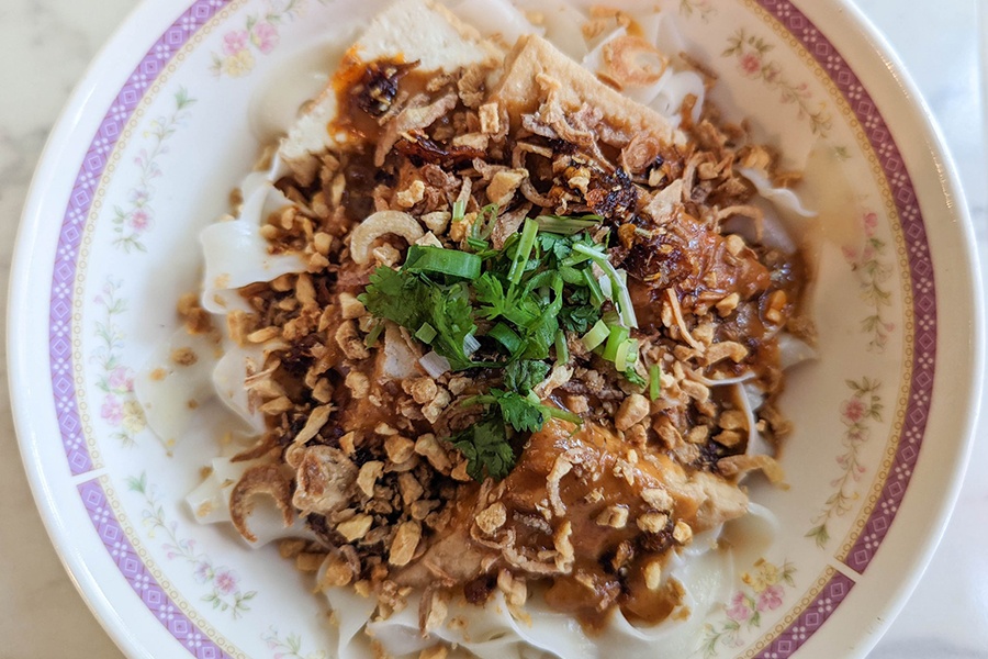 Overhead view of a bowl of medium-width rice noodles topped with a peanut sauce and chopped scallions.