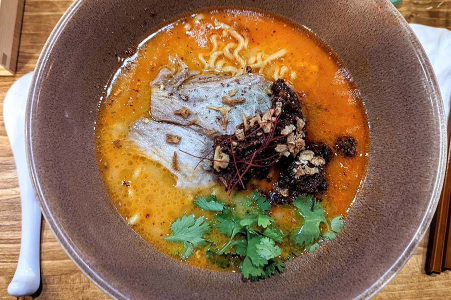 Overhead view of a bowl of ramen with a thick, orange broth, slices of meat, and ground pork.