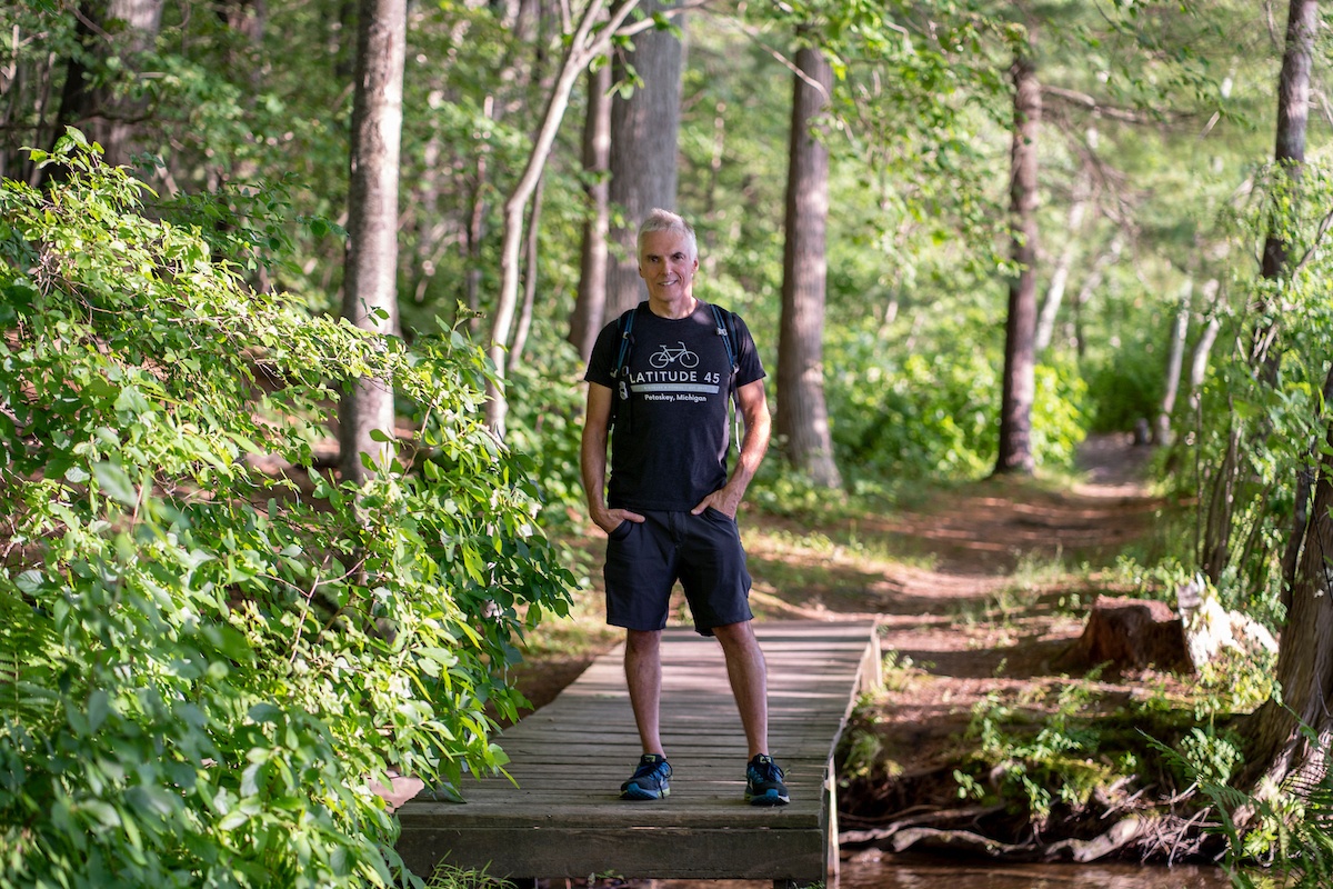 Author Jay Atkinson stands on a bridge in a forest.