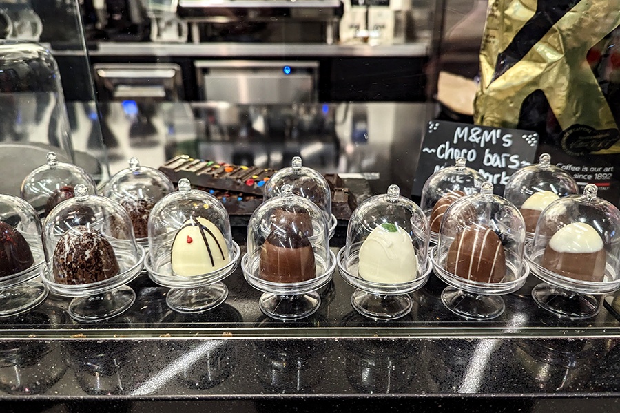 A variety of chocolate bonbons, each in its own little glass cloche, on a cafe counter.