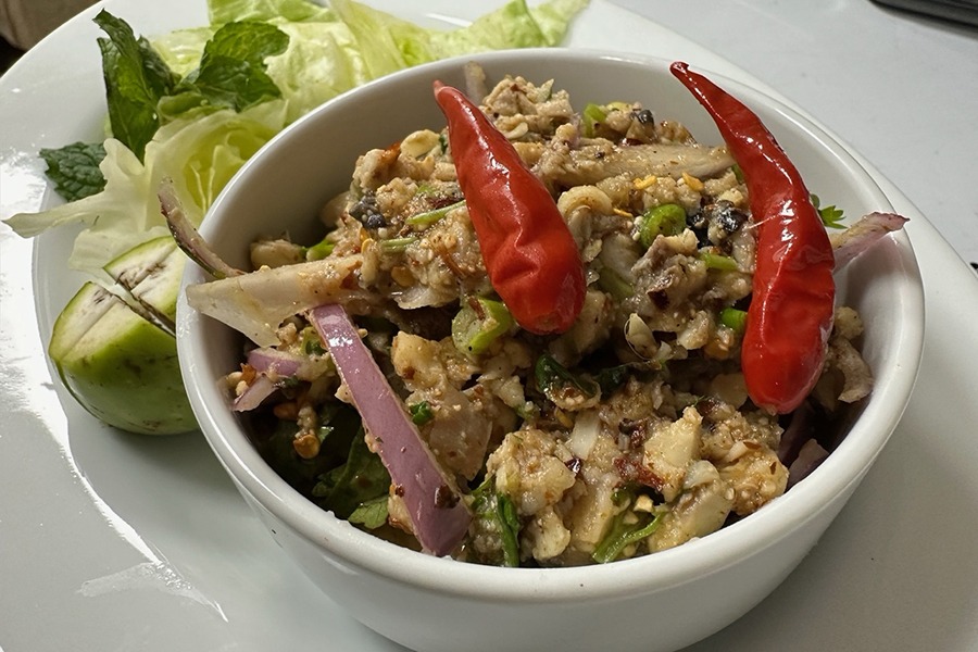 Closeup on a northern Thai salad of ground catfish with herbs, shallots, and chilis, served in a small white bowl.