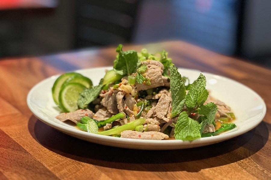 A Thai dish features thin slices of pork in a salad full of fresh mint and lime slices.