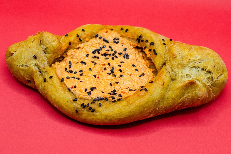 A sort of diamond-shaped open pastry has a filling of a red peppery feta with black sesame seeds.