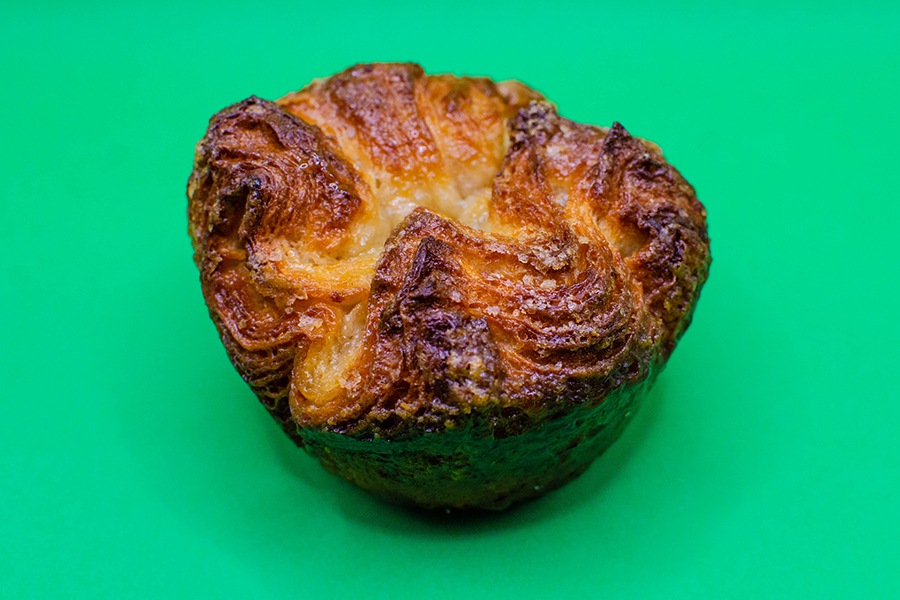 A crown-shaped laminated pastry with a sugary exterior sits on a green background.