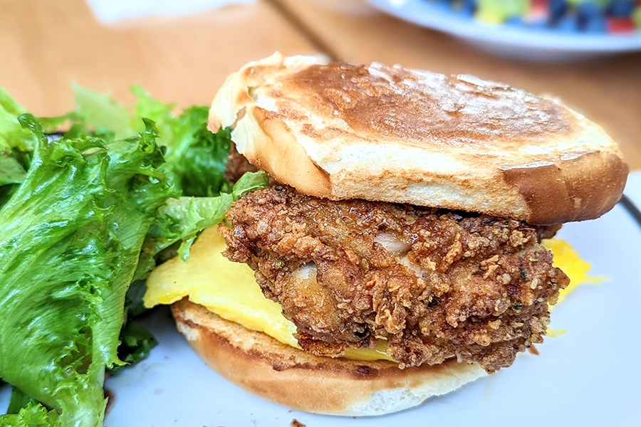 Fried chicken sits on an egg on a thin bun with a side of leafy greens.