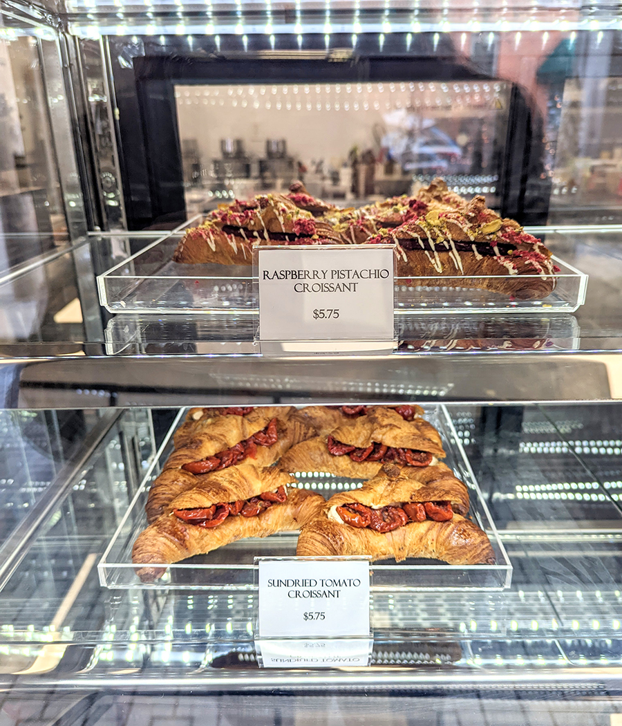 Filled croissants are in a pastry display case inside a bakery.