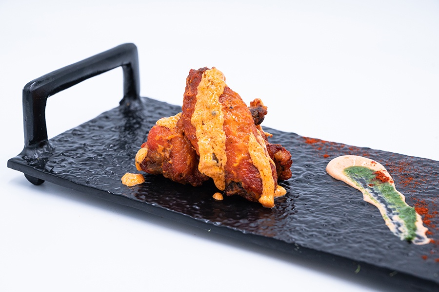 Several chicken wings are displayed on a rectangular black platter, garnished with strips of a thick orange sauce.