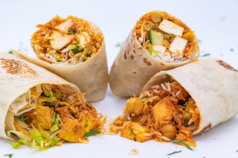 Two wraps are cut in half, stuffed with rice, chickpeas, paneer, and other fillings.