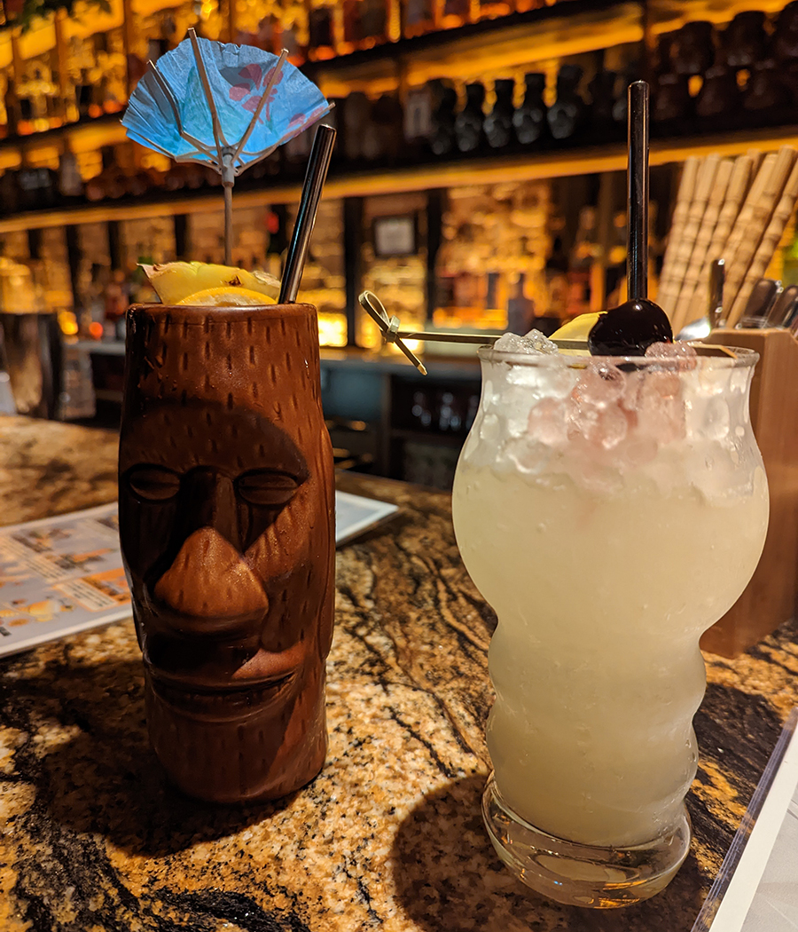 Two cocktails in tiki-style glassware sit on a marble bar.