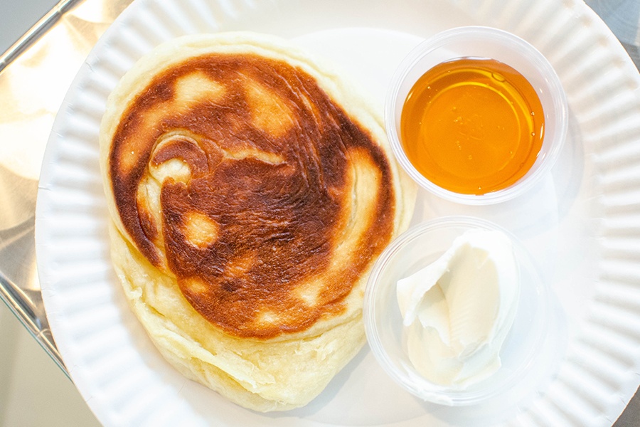A browned round of flatbread is served with sides of honey and cream cheese.