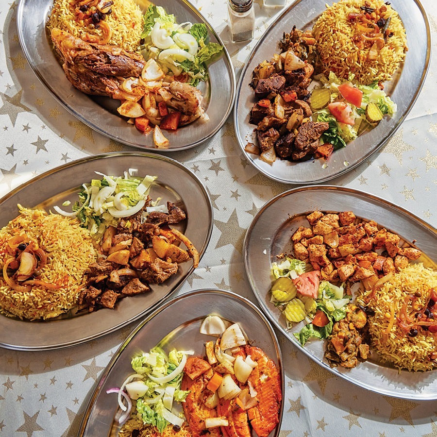 Overhead view of five hearty dishes of meats, rice, and salad at a Middle Eastern restaurant, laid out across a tablecloth with silver stars on it.