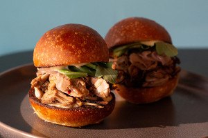 Two sliders sit on a plate, filled with a pulled meat substitute and arugula.