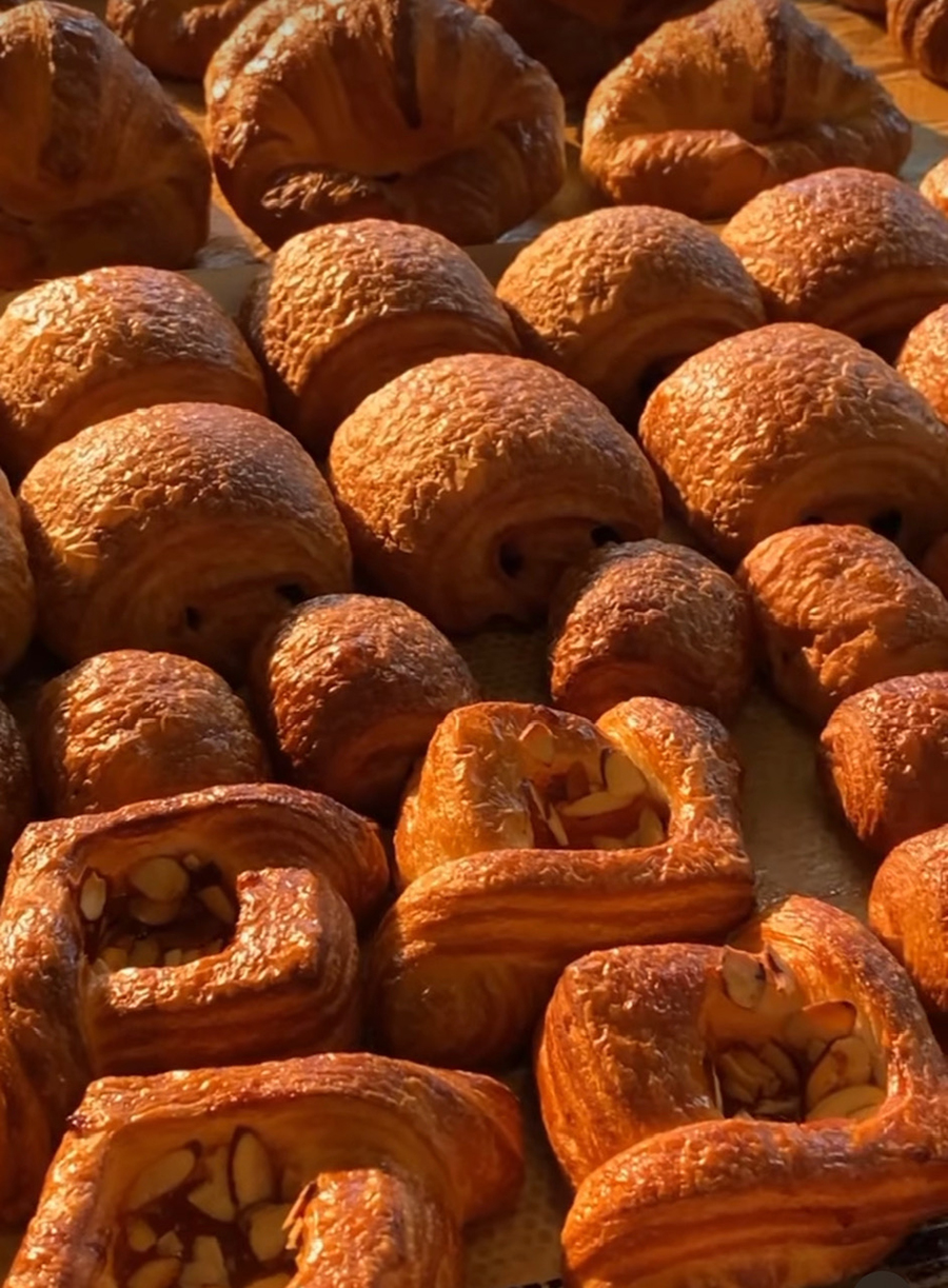 Several rows of golden-brown croissants in a variety of styles.