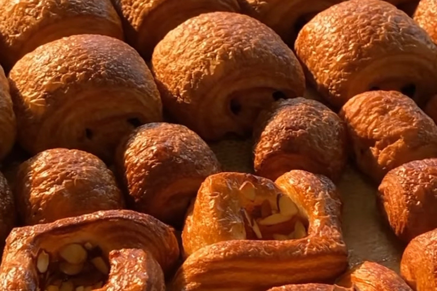 Several rows of golden-brown croissants in a variety of styles.