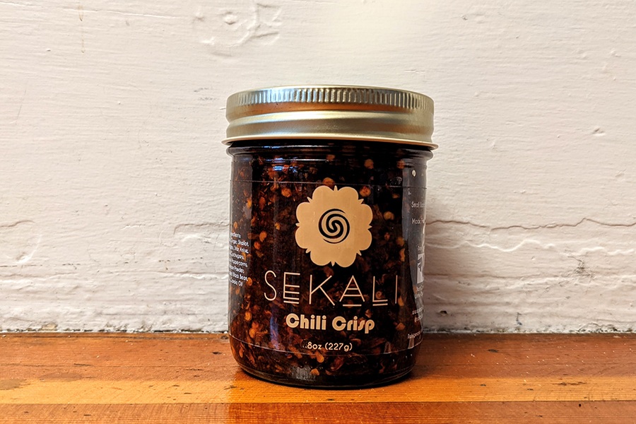 A jar labeled Sekali Chris Crisp is full of a dark red condiment.