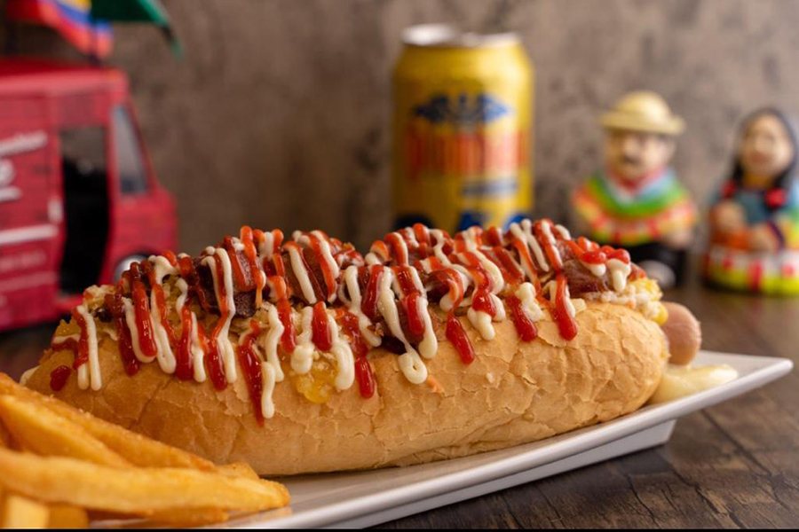 A large hot dog is covered with thick squiggles of ketchup and mayo.