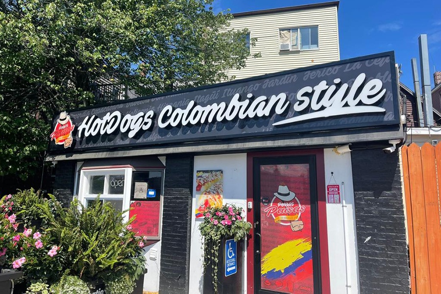 A small, one-story restaurant has large signage reading Hot Dogs Colombian Style.