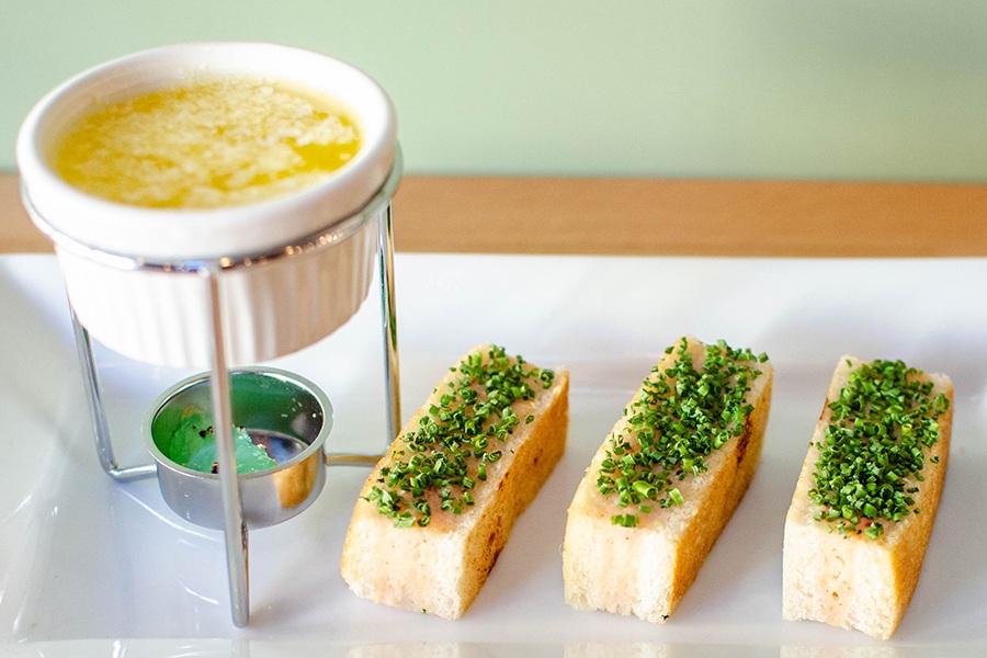 Three finger sandwiches are garnished with chopped chives and a ramekin of melted butter.