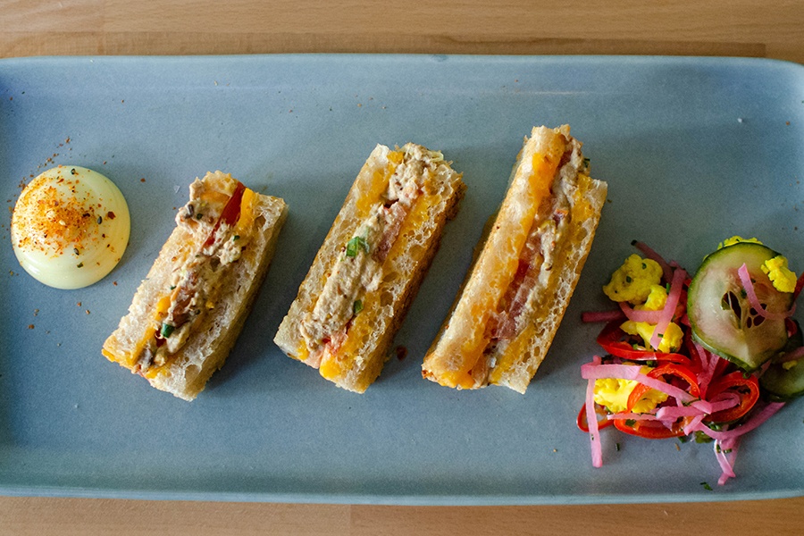 Three finger sandwiches are displayed on a blue plate with a side of colorful pickled vegetables.