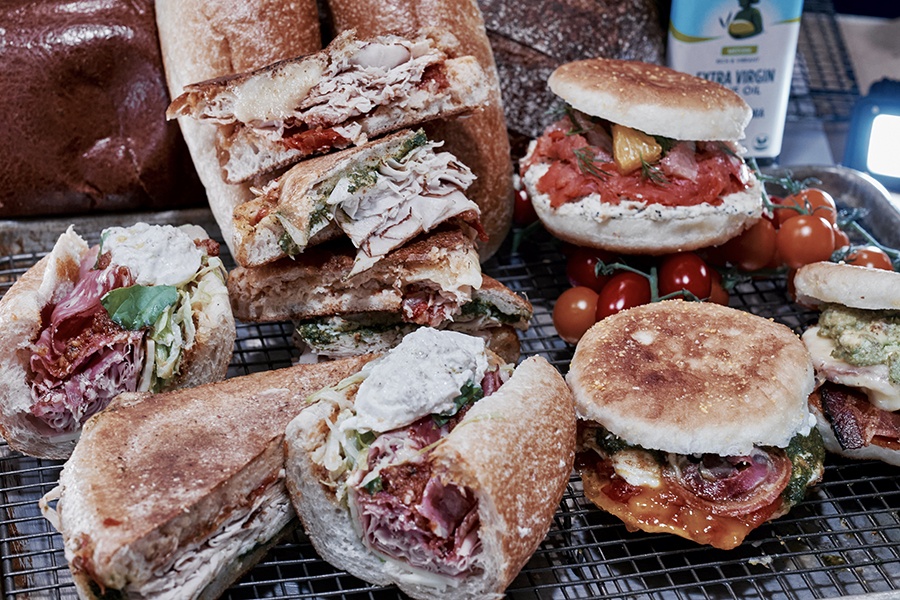 A variety of deli sandwiches, stuffed full of thinly sliced meats, are displayed on a cooking rack.
