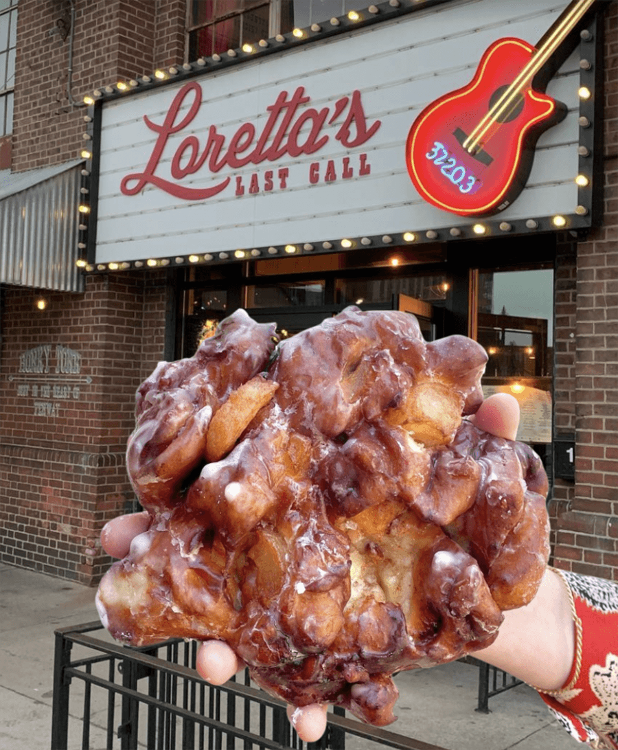 A hand holds up a giant pastry in front of a sign that says Loretta's Last Call.