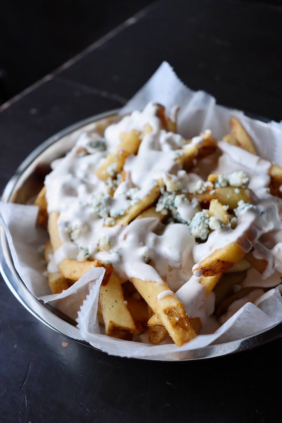 Fries are smothered in a creamy white sauce with chunks of blue cheese visible on top.