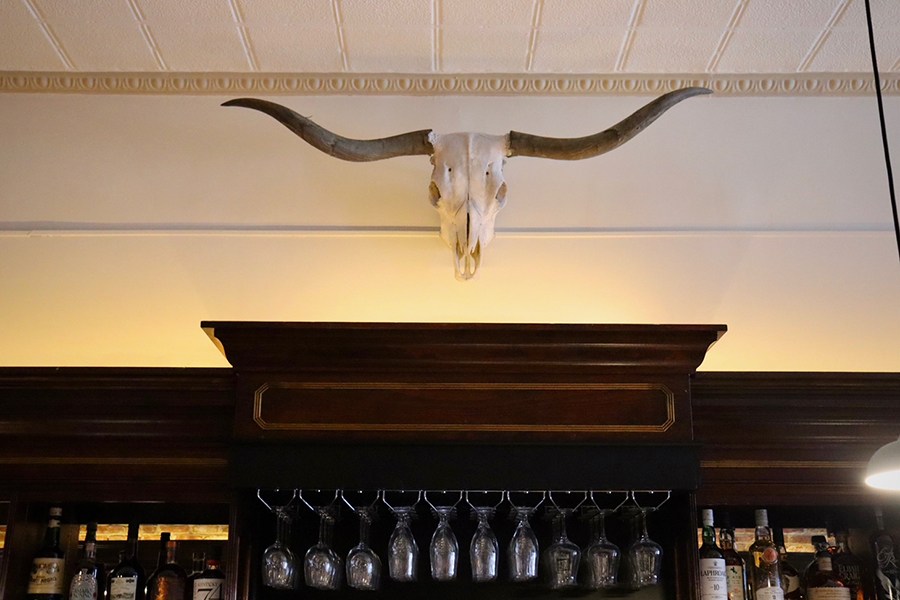 A steer skull is displayed above a dark wooden bar in a restaurant.