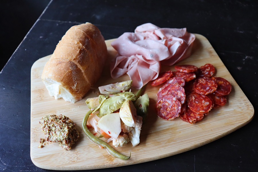 Meats, mustard, and bread are arranged on a wooden board.