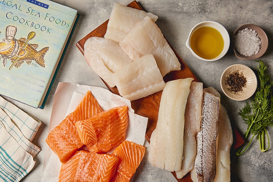 Overhead view of raw salmon, cod, and haddock filets next to a seafood cookbook.