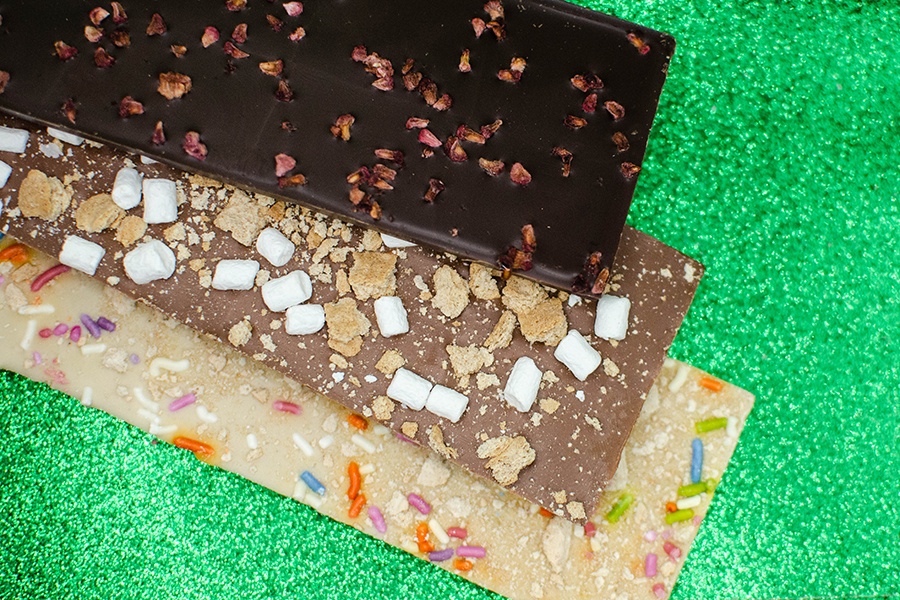 Three chocolate bars of different flavors are displayed on a sparkly green background.