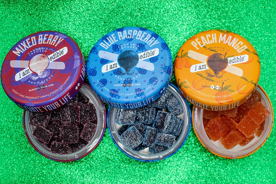 Three round tins with a hot air balloon logo are open to reveal three different flavors of cannabis-infused gummies.