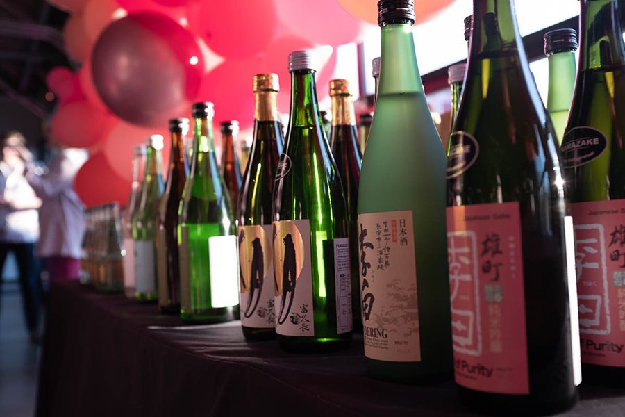 Bottles of sake are lined up on a table, with pink balloons visible in the background