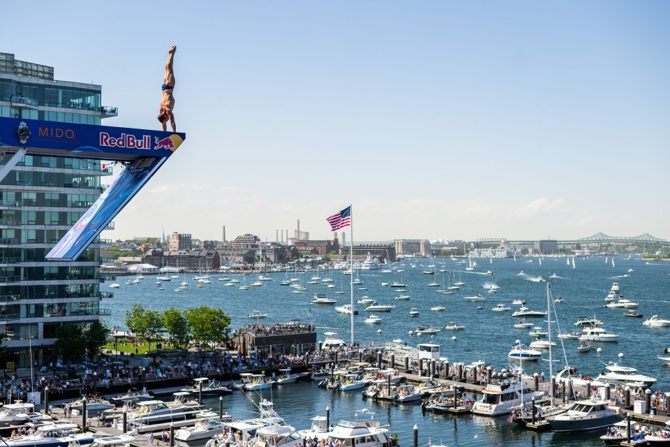 Ritratto di un uomo atletico in piedi in punta di piedi alla fine di un trampolino eretto al largo della costa del porto di Boston.