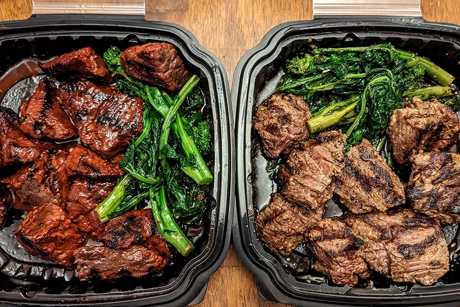 Two takeout containers of steak tips with sides of broccolini. One portion of tips has a reddish marinade.