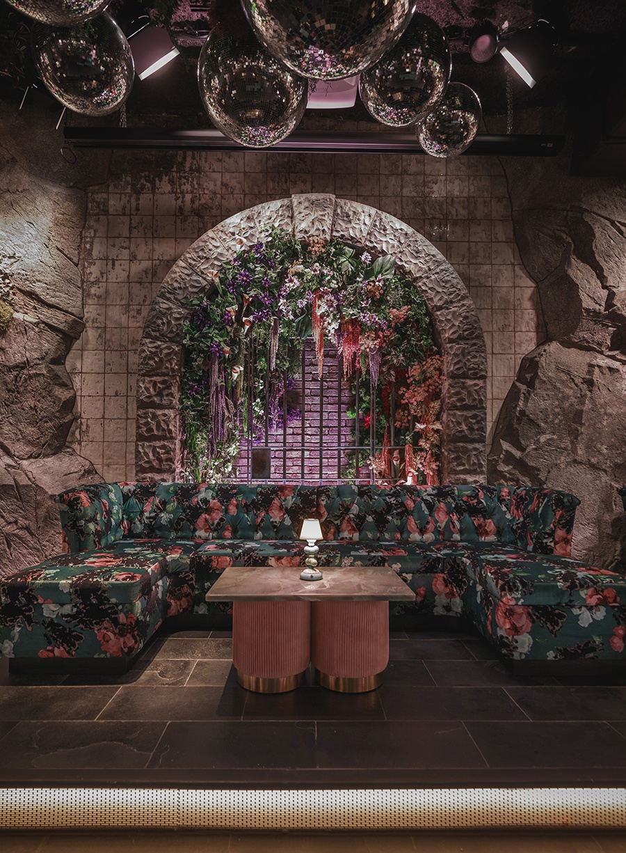 Couches with tropical leaf patterns sit in a dimly lit, cave-like nightclub setting.
