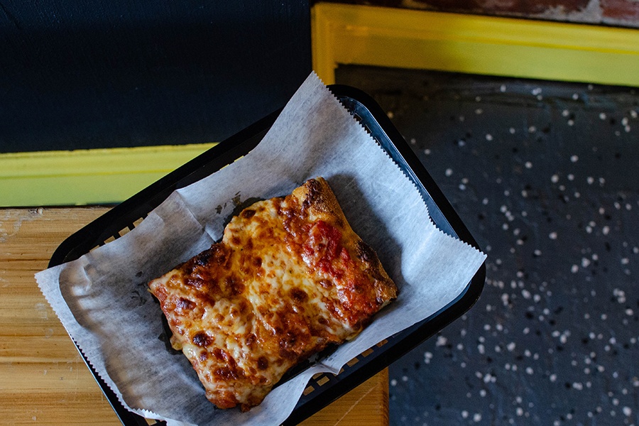 Overhead view of a rectangular slice of cheese pizza on a light wooden table.
