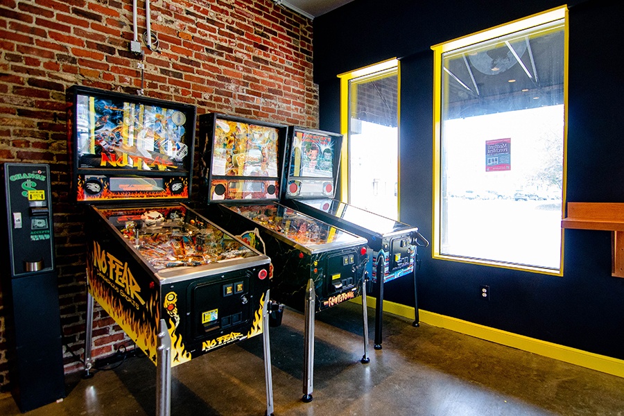 A row of three pinball machines and a change machine in front of a brick wall.
