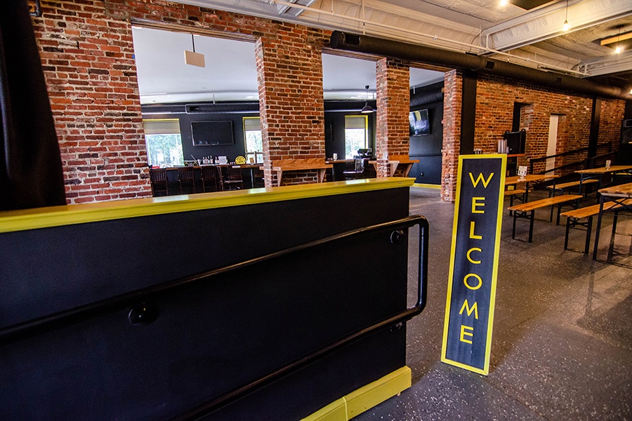 A black-and-yellow sign at the front of a restaurant space says welcome, with picnic-style tables visible in the background.