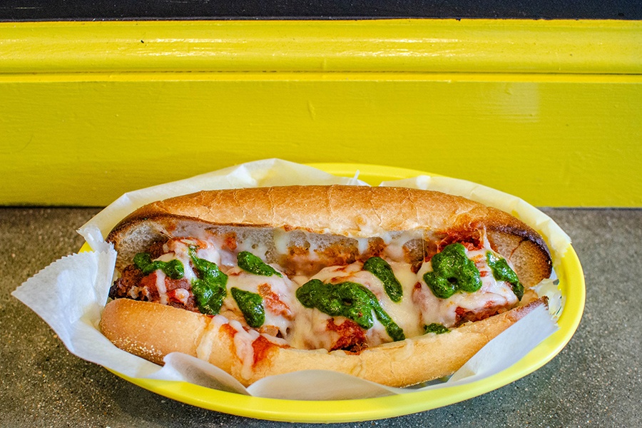 Meatballs on a sub roll are covered with melted cheese and a drizzle of pesto.