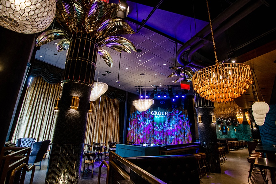 A jazz club features a variety of eye-catching light fixtures and gold palm leaves at the top of large black columns.