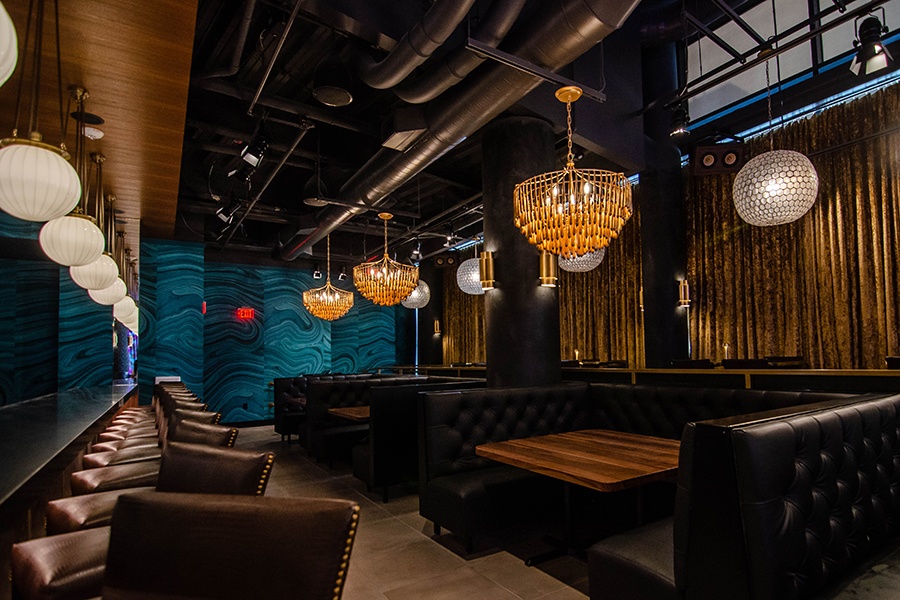 A bar and restaurant features dark brown leather seating, heavy velour curtains, and green wallpaper that looks like the inside of an agate.