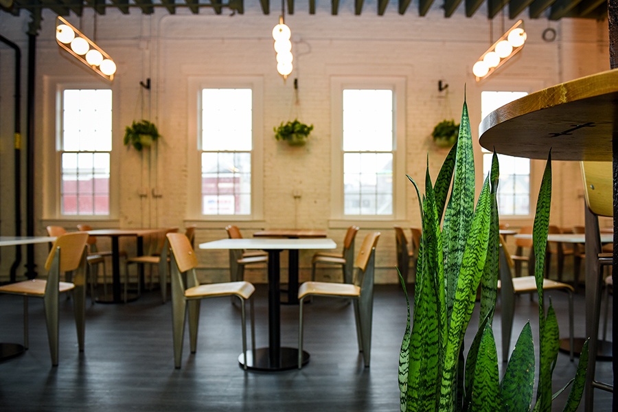 A white-brick taproom is filled with small tables and a handful of plants.